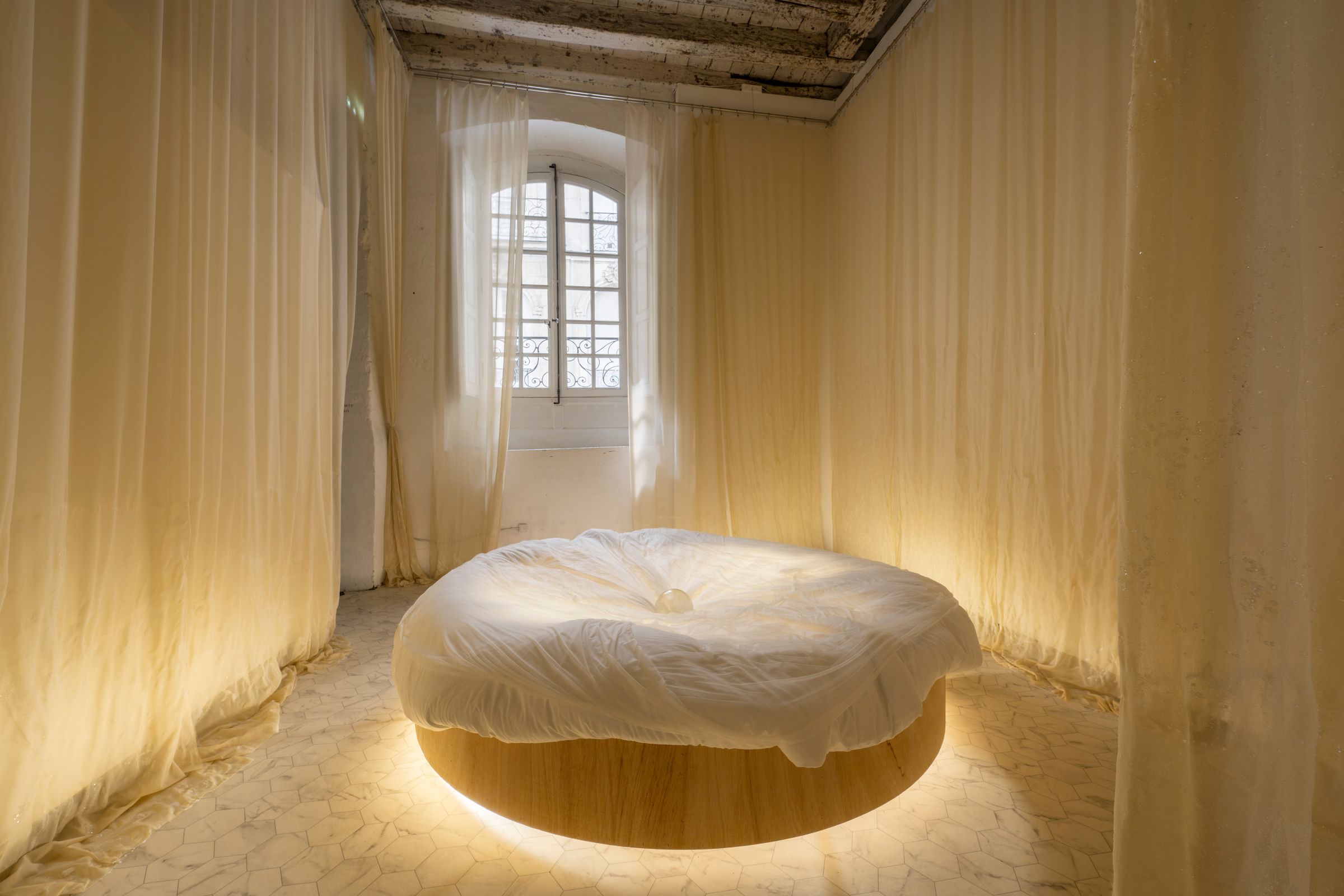 The Faint House of YES, 2021 Site specific installation :  le Voyage de Nantes, France.   Mixed media, (watermarked and crystallised curtains, round bed, neon, crystal ball, marble imitation floor)  © Martin Argyroglo/ le Voyage de Nantes